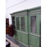 A GREEN PAINTED BREAKFRONT BOOKCASE WITH GREY DETAILS, THE UPPER HALF GLAZED AND THE BASE WITH