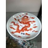 A CHINESE PLATE PAINTED IN IRON RED WITH A DRAGON, FOUR CHARACTER MARK. Dia. 21cms.