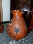 A TERRACOTTA JUG DECORATED WITH BLACK CENTRED FLOWERS. H 45cms