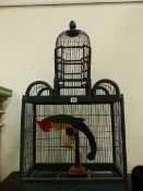 A KHAKI PAINTED WOOD AND WIRE BIRD CAGE HOUSING A WOODEN PARROT