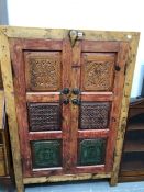 AN INDIAN PINE CUPBOARD, EACH OF THE THREE PANELS TO THE DOORS CARVED AND COLOURED AND ENCLOSING
