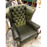 A GREEN LEATHER BUTTON BACKED WING ARM CHAIR ON MAHOGANY CABRIOLE LEGS WITH CLUB FEET.