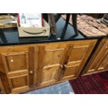 TWO SIMILARLY BLACK IGNEOUS STONE TOPPED PINE CABINETS, ONE WITH TWO DOORS AND THE OTHER WITH THREE.