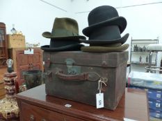 A LEATHER HAT BOX, FOUR TRILBYS AND A BOWLER HAT.