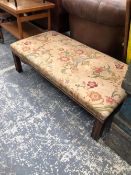 A MAHOGANY OTTOMAN, THE CLOSE NAILED FLORAL UPHOLSTERED SEAT ON MAHOGANY CHANNELLED SQUARE SECTIONED