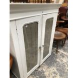 A CREAM PAINTED CABINET WITH TWO GLAZED DOORS ENCLOSING FOUR SHELVES. W 102 x D 37 x H 119.5cms.