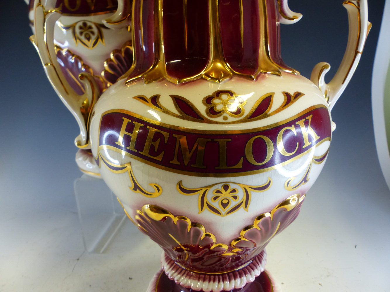 A PAIR OF POTTERY TWO HANDLED BALUSTER JARS AND COVERS LABELLED HEMLOCK AND CLOVES IN GILT ON A WINE - Image 3 of 4