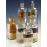 SIX CLEAR GLASS PHARMACY BOTTLES AND FIVE STOPPERS, EACH OF THE CYLINDRICAL BODIES LABELLED IN BLACK