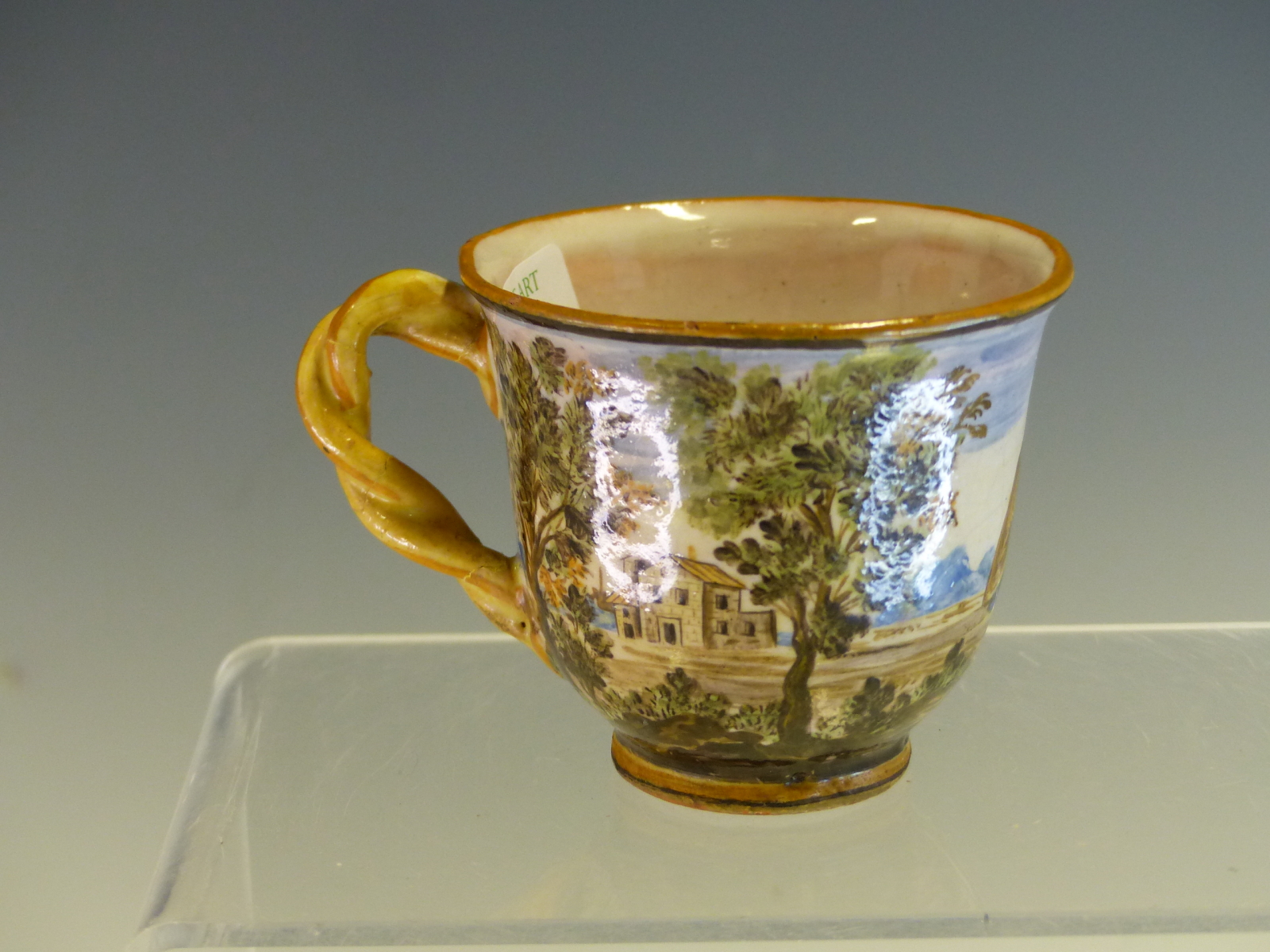 A MID 18th C. CASTELLI MAIOLICA COFFEE CUP PAINTED WITH A WAYFARER AMONGST TREES WITH DISTANT