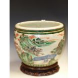 A CHINESE FAMILLE VERTE PLANTER AND WOOD STAND, THE ROUNDED EXTERIOR OF THE FORMER PAINTED WITH