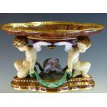 A MID VICTORIAN MINTON MAJOLICA BROWN AGATE WARE TAZZA SUPPORTED ON THE BACKS OF TWO AMORINI BACK TO