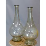 TWO SIMILAR CLEAR GLASS FLASK, THE WATER DROP SHAPES ON SOCLE FEET. H 64 AND 62cms