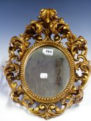 AN OVAL MIRROR IN A FLORENTINE GILT FRAME PIERCED AND MOULDED WITH FOLIAGE ENCLOSING A BEAD BAND.