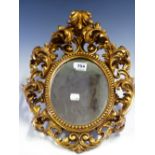 AN OVAL MIRROR IN A FLORENTINE GILT FRAME PIERCED AND MOULDED WITH FOLIAGE ENCLOSING A BEAD BAND.