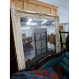 A RECTANGULAR BEVELLED GLASS MIRROR, THE CREAM PAINTED FRAME WITH FOLIAGE MOULDINGS AT THE CORNERS