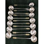 THIRTEEN EUROPEAN WHITE METAL SPOONS WITH THE LONG HANDLES TO THE ROUND BOWLS TOPPED BY GILT PAIRS