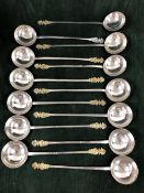 THIRTEEN EUROPEAN WHITE METAL SPOONS WITH THE LONG HANDLES TO THE ROUND BOWLS TOPPED BY GILT PAIRS