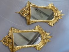 A PAIR OF LATE VICTORIAN ROUND ARCH WALL MIRRORS IN GILT GESSO AND CARVED WOOD FRAMES CRESTED BY FE