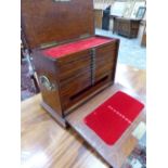 A LATE 19th C. OAK COLLECTORS CABINET CONTAINING TWELVE RED VELVET LINED TRAYS OVER A DEEPER DRAWER.