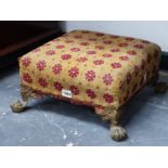 AN ANTIQUE UPHOLSTERED FOOT STOOL ON BRASS BALL AND CLAW FEET.