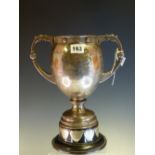 A TWO HANDLED BALUSTER TROPHY CUP AND SHIELD MOUNTED WOOD STAND BY WAKELEY AND WHEELER, DUBLIN 1927,