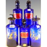 THREE BLUE GLASS PHARMACY BOTTLES AND STOPPERS, THE CYLINDRICAL SHAPES GILT WITH THE ROYAL ARMS