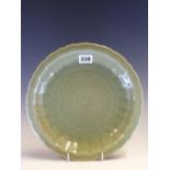 A CHINESE LONGQUAN CELADON DISH, THE FLUTED CAVETTO INCISED WITH FLOWERS WITHIN THE BARBED RIM. Dia.