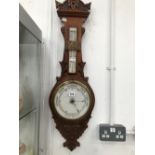 AN ANEROID BAROMETER MOUNTED BELOW A MERCURY THERMOMETER IN A CARVED OAK BANJO CASE