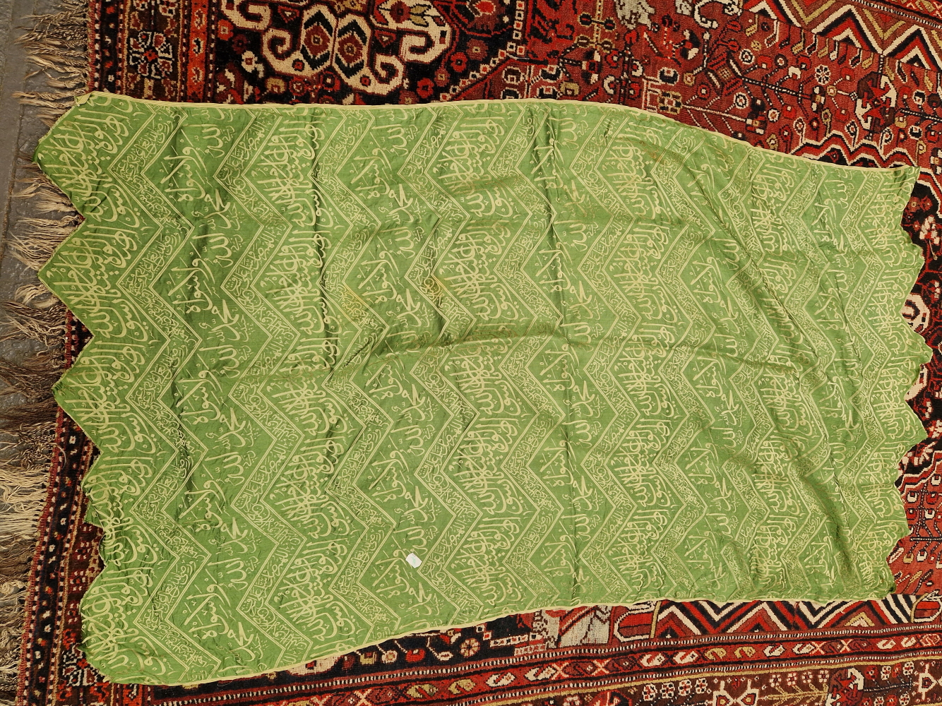 AN ISLAMIC GREEN SILK PANEL WOVEN IN SILVERY GREY WITH CHEVRON BANDS OF SCRIPT. 148 x 84cms.