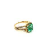 AN 18ct HALLMARKED GOLD EMERALD AND DIAMOND RING. THE EMERALD IN A RAISED FOR CLAW SETTING WITHIN