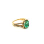 AN 18ct HALLMARKED GOLD EMERALD AND DIAMOND RING. THE EMERALD IN A RAISED FOR CLAW SETTING WITHIN