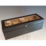 A BLACK LEATHER MOUNTED BOX WITH A GLAZED LID OVER FOUR COMPARTMENTS FOR WRISTWATCHES, EACH WITH