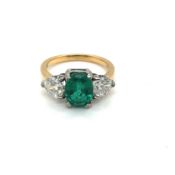 A 18ct GOLD HALLMARKED EMERALD AND DIAMOND RING. THE OVAL EMERALD FLANKED BY HEART CUT DIAMONDS.
