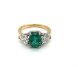 A 18ct GOLD HALLMARKED EMERALD AND DIAMOND RING. THE OVAL EMERALD FLANKED BY HEART CUT DIAMONDS.