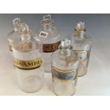 FIVE CLEAR GLASS PHARMACY BOTTLES AND STOPPERS, THREE BEING LABELLED WITH PAPER AND TWO WITH