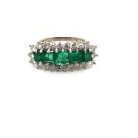 AN EMERALD AND DIAMOND GRADUATED CLUSTER RING. THR FIVE PRINCESS CUT EMERALDS  SURROUNDED BY A FRAME