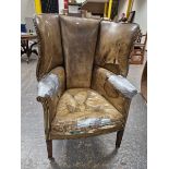 AN ANTIQUE LEATHER UPHOLSTERED WING ARMCHAIR WITH THE BACK ROUNDING OVER THE ARMS, THE SQUARE