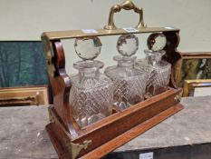 A 19th C. OAK THREE BOTTLE TANTALUS WITH BRASS HANDLED LOCKING PLATE AND CORNER BRACKETS. W 37cms.