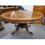 A VICTORIAN WALNUT SHAPED OVAL TABLE, THE QUARTER VENEERED TOP ON FOUR BRACKETS MEETING LEGS WITH