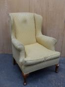 A GEORGIAN STYLE WING ARMCHAIR UPHOLSTERED IN YELLOW GROUND MATERIAL ABOVE WALNUT CABRIOLE FRONT
