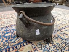A BRONZE THREE LEGGED CAULDRON, THE RIM FLARING FROM THE BODY AND OVER SWUNG BY AN IRON HANDLE. Dia.