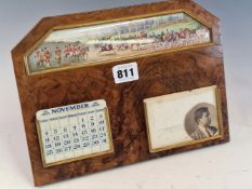 AN EASEL BACKED WALNUT CALENDAR WITH IVORINE INTERCHANGEABLE DATES BELOW A PAINTED SCENE OF A HUNT