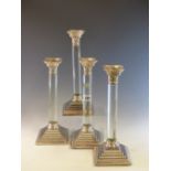 A SET OF FOUR ELECTROPLATE CANDLESTICKS, THE GLASS COLUMNS WITH CORINTHIAN CAPITALS AND BEADED