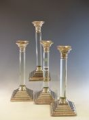 A SET OF FOUR ELECTROPLATE CANDLESTICKS, THE GLASS COLUMNS WITH CORINTHIAN CAPITALS AND BEADED