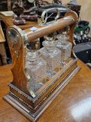 A LATE 19th/EARLY 20th C. OAK THREE BOTTLE TANTALUS WITH NICKEL MOUNTS ABOVE BATON AND REEL CARVED