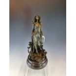 A COLD CAST BRONZE FIGURE OF AN ART NOUVEAU LADY STANDING AMONGST AND DRAPED WITH LILIES, HER EYES C