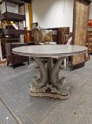 A CONTEMPORARY SILVERED CIRCULAR TABLE SUPPORTED ON A THREE DOLPHIN COLUMN AND TRIPARTITE FOOT. Dia.