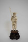 Ivory okimono figure of a fisherman, Meiji period, on carved wooden stand, 14cm high