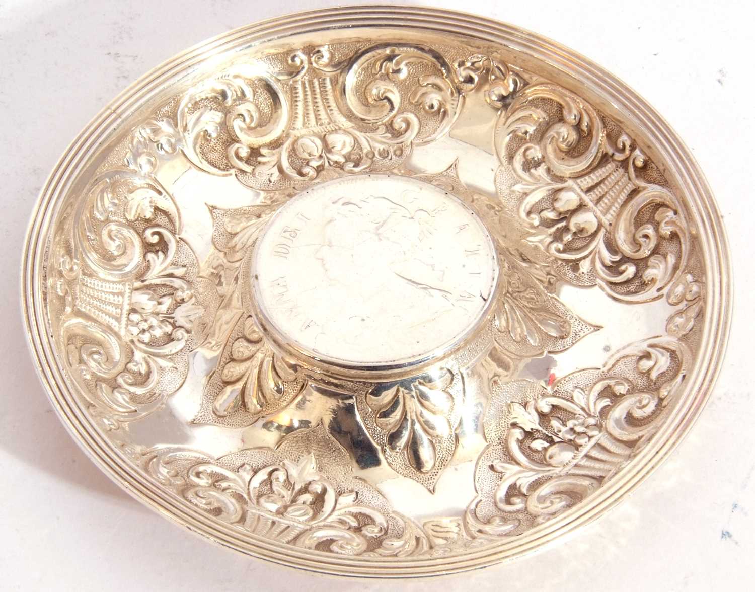 White metal dish of circular form, embossed with baskets of flowers, the centre raised with a 1707
