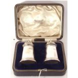 Cased heavy pair of George V peppers of castle type with pierced domed lids and urn finials, 8cm